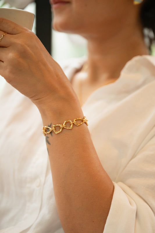 Woman holding a cup with a gold bracelet on her wrist, wearing a white dress.