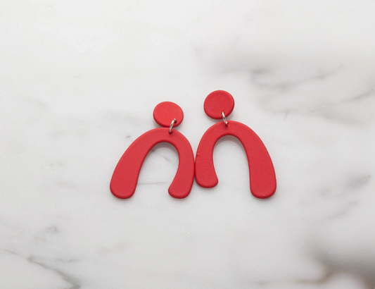 Red arch-shaped earrings on a marble surface